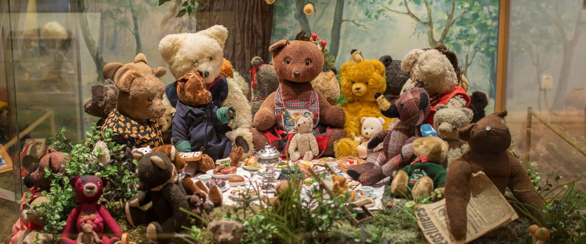 This image shows a collection of vintage teddy bears set up for a picnic tea party, currently on display at the Tartu Toy Museum in Estonia.