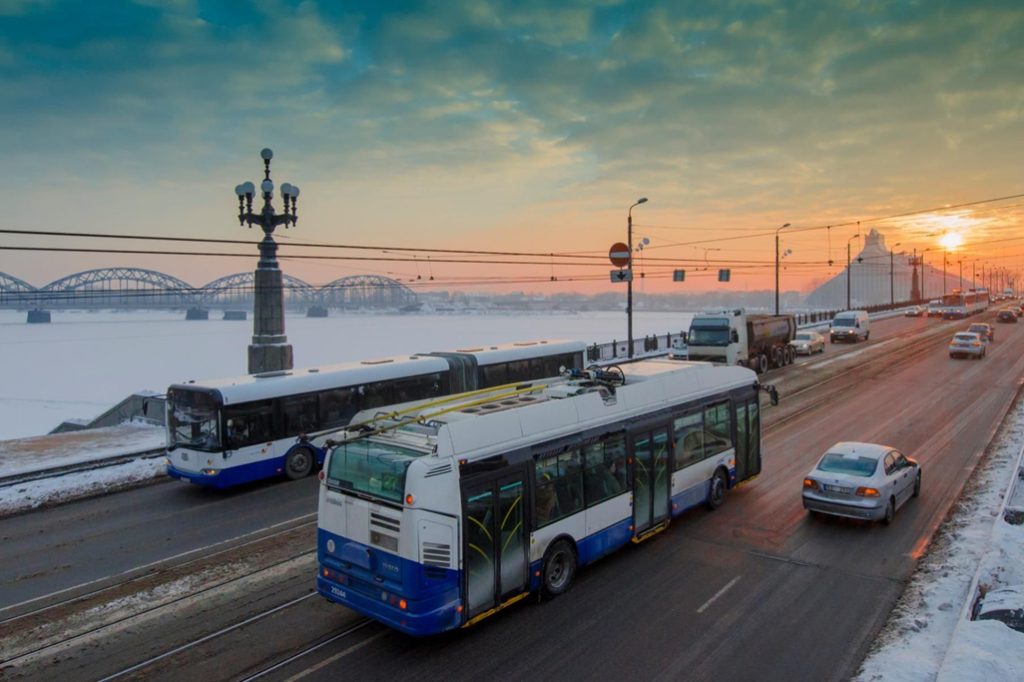 Buses and cars crossing a bridge in Riga at sunset.