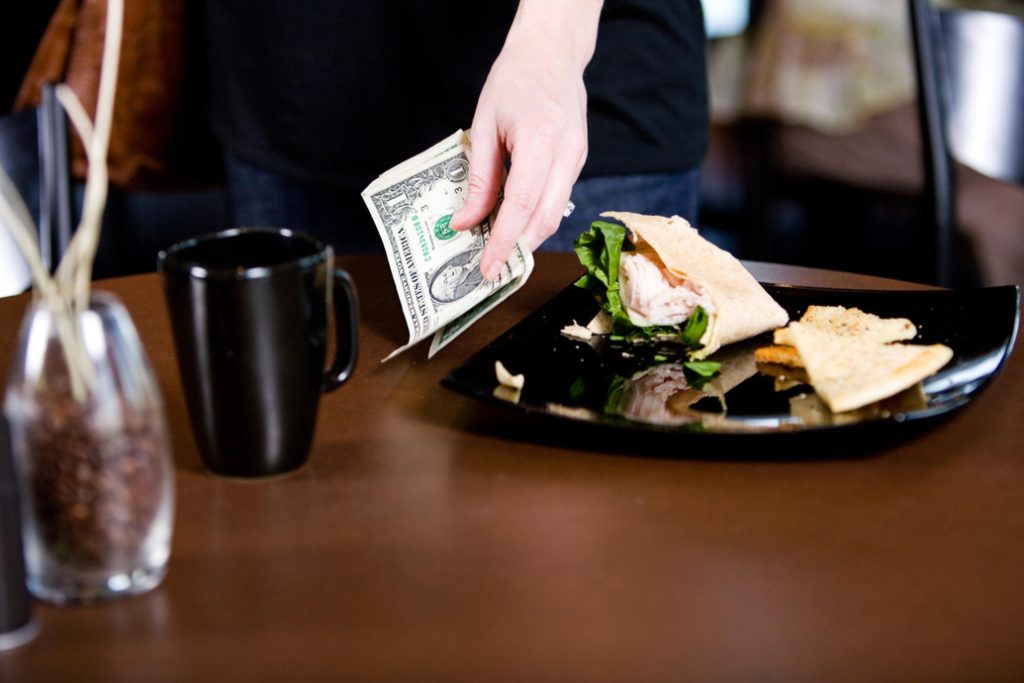 Person leaving a cash tip in US dollars at a restaurant.