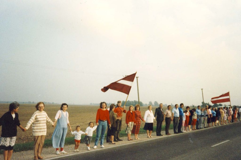 People holding hands along a road with Latvian flags during the Baltic Way.