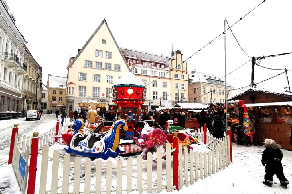Snow-covered Christmas market with children's rides in Tallinn.